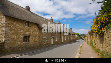 Panoramablick auf die Reihe der strohgedeckten Steinhäusern im historischen Dorf Abbotsbury, Dorset, England unter blauen Himmel Stockfoto