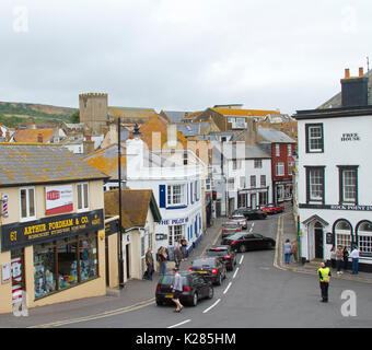 Staus, bei der die Zeile der Autos an der roten Ampel in der schmalen Straße zwischen hohen Gebäuden in Lyme Regis, Dorset, England Stockfoto