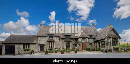 Panoramablick auf historischen des 17. Jahrhunderts Wagen und Pferde Pub, mit Strohdach und Steinmauern unter blauem Himmel, Beckhampton, England Stockfoto