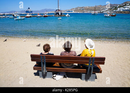 Drei Frauen sitzen auf einer Bank mit Blick auf den Alten Hafen, Mykonos, Griechenland. Stockfoto