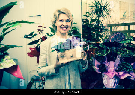 Lächelnde ältere Frau mit floralen Komposition in den Händen im Blumengeschäft Stockfoto