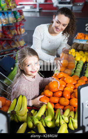 Fröhliche junge Frau und kleines Mädchen Einkauf süßen Mandarinen am Markt. Fokus auf Mädchen Stockfoto