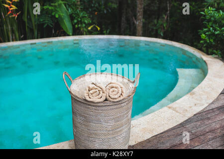 Zwei beige gerollte Handtücher in Weidenkorb in der Nähe von privaten Pool mit türkisklarem Wasser Stockfoto