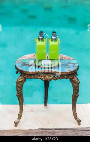 Zwei Flaschen Shampoo und handgemachte Seife auf alte kleine Vintage lackiert Tisch in der Nähe von privaten Luxus Pool. Dusche und Wellness-Set im Hotel Stockfoto