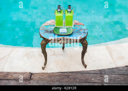 Zwei Flaschen Shampoo und handgemachte Seife auf alte kleine Vintage lackiert Tisch in der Nähe von privaten Luxus Pool. Dusche und Wellness-Set im Hotel Stockfoto