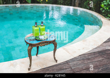 Zwei Flaschen Shampoo und handgemachte Seife auf alte kleine Vintage lackiert Tisch in der Nähe von privaten Luxus Pool. Dusche und Wellness-Set im Hotel Stockfoto