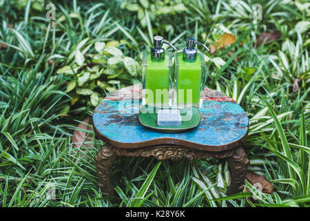 Zwei Flaschen Shampoo und handgemachte Seife auf alte kleine Vintage lackiert Tabelle im grünen Garten. Dusche und Wellness-Set im Hotel Stockfoto