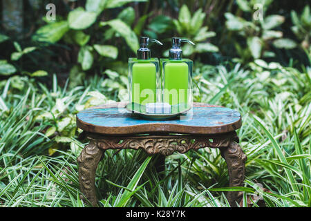 Zwei Flaschen Shampoo und handgemachte Seife auf alte kleine Vintage lackiert Tabelle im grünen Garten. Dusche und Wellness-Set im Hotel Stockfoto