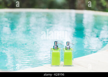 Zwei Flaschen Shampoo und handgemachte Seife am Rande der Pool mit Türkis und transparente sauberes Wasser. Stein und Holz- Hintergrund. Dusche und Spa kit i Stockfoto