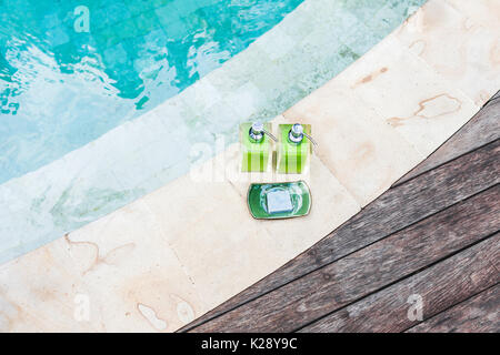 Zwei Flaschen Shampoo und handgemachte Seife am Rande der Pool mit Türkis und transparente sauberes Wasser. Stein und Holz- Hintergrund. Dusche und Spa kit i Stockfoto