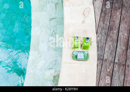 Zwei Flaschen Shampoo und handgemachte Seife am Rande der Pool mit Türkis und transparente sauberes Wasser. Stein und Holz- Hintergrund. Dusche und Spa kit i Stockfoto