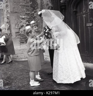 1964, historische, Hochzeit, zwei Blume Mädchen mit Braut und Bräutigam vor dem Eingang zur Kirche nach der Hochzeit cermony, England, UK. Stockfoto