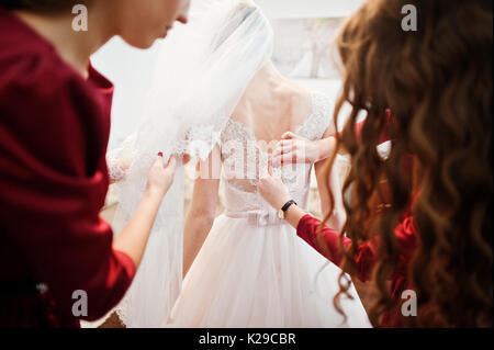 Brautjungfern helfen Braut einen Bogen auf einer Hochzeit Kleid zu binden. Stockfoto