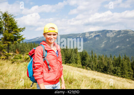 Junge lächelnde Mädchen im Teenageralter mit Rucksack mit Blick in die Berge. Sommerurlaub Wandern Konzept Hintergrund mit Kopie Raum Stockfoto