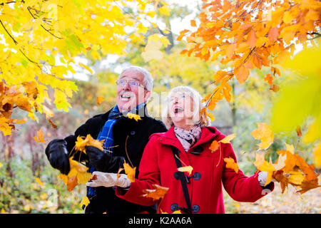 Ältere Paare sind auf einen Herbst Spaziergang im Wald. Sie herauf die Blätter und warf sie in die Luft um sie herum. Stockfoto