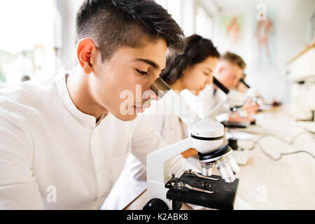 Schöne High School Kursteilnehmer mit Mikroskopen im Labor. Stockfoto