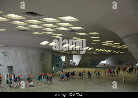 Große Gruppe von Kindern tragen orangefarbenen Kappen Spaziergang unter den Wissenschaftszentrum Phaeno von Irakischen konzipiert - geborene britische Architektin Zaha Hadid in Wolfsburg, Niedersachsen, Deutschland. Stockfoto