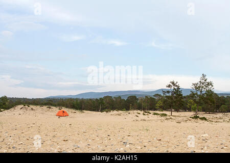 Touristische Zelt auf dem Sandstrand am Ufer des Baikalsees in Sibirien im Sommer unter den Nadelbäumen auf einem Berg im Hintergrund. Stockfoto