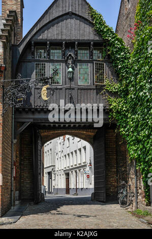 Die schwarze Holz verkleideten Gebäude über einem Torbogen in der mittelalterlichen Stadt Brügge/Brügge in Belgien im Sommer Sonnenschein mit einem Gold half moon Emblem Stockfoto
