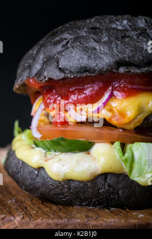 Frische leckere Burger auf schwarzem Hintergrund. Hausgemachte Hamburger mit Rindfleisch, Zwiebeln, Tomaten, Salat und Käse mit Zutaten Stockfoto