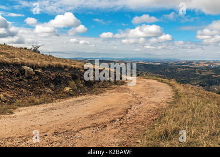 Gebogene ländlichen unbefestigte Straße durch trockenes Gras gegen hiils Täler und blauen bewölkten Himmel Landschaft am Lake Eland Game Reserve in KwaZulu-Natal in Süd Afri Stockfoto