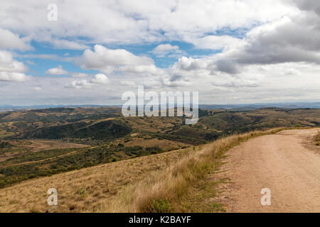 Gebogene ländlichen unbefestigte Straße durch trockenes Gras gegen hiils Täler und blauen bewölkten Himmel Landschaft am Lake Eland Game Reserve in KwaZulu-Natal in Süd Afri Stockfoto