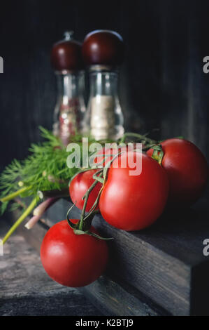 Rote Tomaten auf einem Zweig liegen auf einem hölzernen Hintergrund im rustikalen Stil Reif, Geräte für die Gewürze in das helle Licht des Morgens. Stockfoto