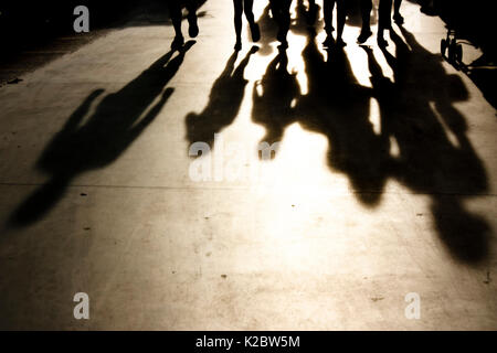 Verschwommene Schatten von Menschen zu Fuß in Richtung der Kamera an der Strandpromenade in misty Sommer Sonnenuntergang in Schwarz und Weiß Stockfoto