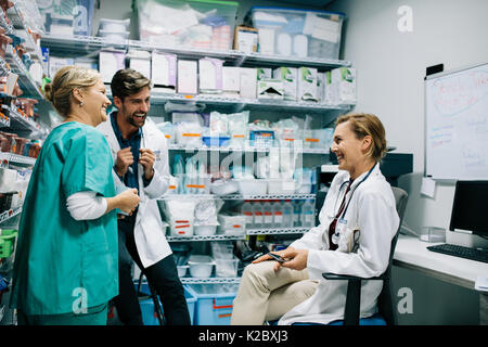Krankenhauspersonal in zwangloser Diskussion in der Apotheke. Drei Kollegen treffen in Apotheke und Lachen. Stockfoto