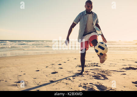 Junger Mann, Fußball spielen, am Meer. Afrikanischer Mann kicken Fußball am Strand. Stockfoto