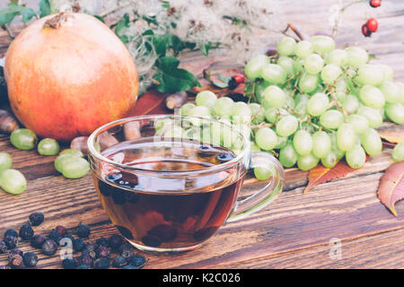 Getränk aus getrockneten Weißdorn-Beeren, ein Bündel aus weißen Trauben und ein Granatapfel auf dem Tisch Nahaufnahme. Gefärbtes Bild. Herbst Konzept Stockfoto