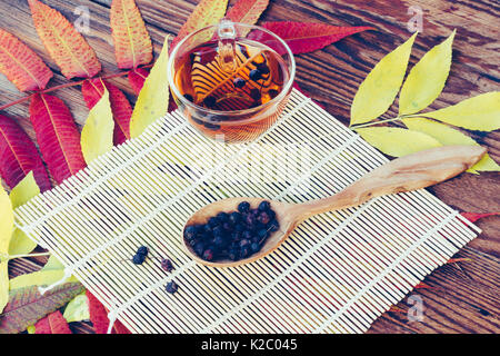 Getränk aus getrockneten Weißdorn-Beeren in hölzernen Löffel auf dem Tisch mit der bunten Blätter im Herbst. Ansicht von oben Nahaufnahme. Gefärbtes Bild. Herbst Konzept Stockfoto