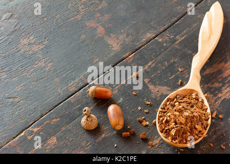 Eicheln und zerdrückten Eichenrinde in einem Löffel aus Holz auf einem alten schwarzen Holztisch. vegetativen Rohstoffe für die Zubereitung von Kaffee Getränke, Arzneimittel Produ Stockfoto