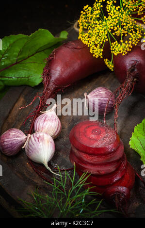 In Scheiben geschnitten Zuckerrüben für die Herstellung von Chips auf einem Holzbrett mit Knoblauch und Dill im rustikalen Stil. Stockfoto