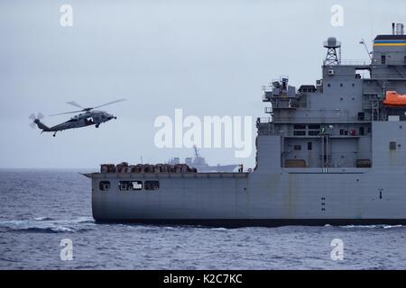 Ein U.S. Navy MH-60S Seahawk Hubschrauber hebt die Lieferungen aus der US-Navy Lewis und Clark-Klasse Dry Cargo Munition ship USNS Matthew Perry 15 August, 2017 im Pazifischen Ozean. Stockfoto