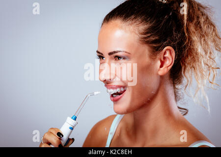 Lächelnde junge Frau mit Klammern ihre Zähne reinigen mit mundirrigator. Stockfoto