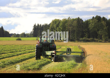 JOKIOINEN, Finnland - 25. AUGUST 2017: Landwirt Schnitte Heu mit Krone EasyCut 3600 CV Mäher von John Deere Traktor auf Spätsommer Abend gezogen. Stockfoto