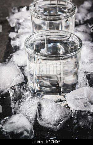 Alkohol und Cocktails. Drei Gläser Wodka auf einer Schiefertafel Fach, mit Eis. Auf einem schwarzen Steintisch, Stockfoto