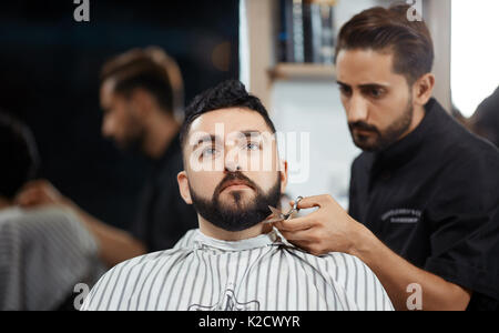Friseur schneiden Brot mit Schere für brunet Mann in Barbershop. Stockfoto