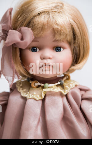 Portrait von Keramik Porzellan handmade Vintage Doll mit Halskette, blonde Haare in alten Bettwäsche rosa kleid mit goldenen gelb Stickereien, Bogen auf Weiß zurück Stockfoto