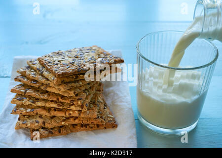Cookies von Blätterteig mit Sesam, Chia und Sonnenblumenkerne mit Milch Ausgießen aus der Flasche mit Glas bedeckt. niedrigen Winkel Stockfoto