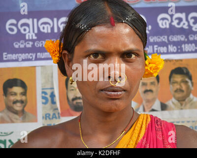 Junge indianische Adivasi-Frau (Mali-Stamm) mit zwei goldenen Nasenringen, Stammesohrringen und zwei gelben Blumen in ihren Haarposalen für die Kamera. Stockfoto