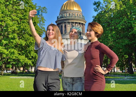 Drei lächelnde Mädchen bilden selfie auf ein Telefon auf dem Hintergrund der St. Isaak Kathedrale Stockfoto