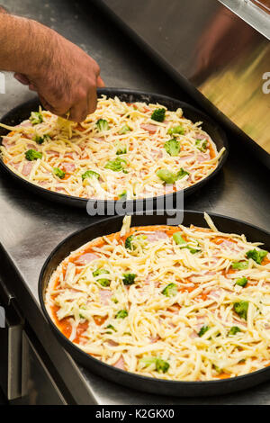 Zwei Black Metal Backbleche mit raw-Pizza auf dem Küchentisch. Die erste Pizza mit Gemüse und geriebenem Käse gemacht, und der zweite mit tomatoe Stockfoto