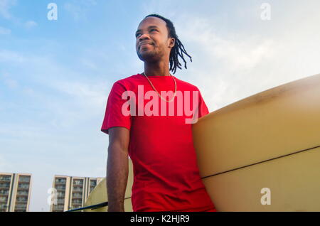 Junge afrikanische amerikanische Mann mit einem Surfbrett draußen Stockfoto