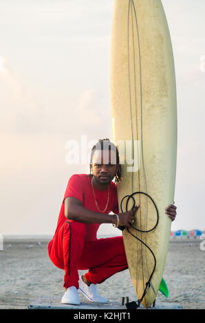 Afrikanische amerikanische Mann mit Surfbrett am Strand Stockfoto