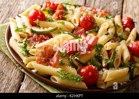 Pasta Penne mit gebratenem Schinken, Tomaten, Zucchini und Käse close-up auf einem Teller. Horizontale Stockfoto