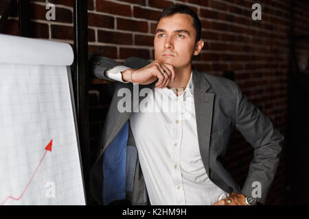 Foto von Business Mann neben Plakat mit Grafik auf Hintergrund der Mauer im Büro Stockfoto