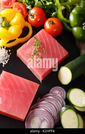 Rohen Rinderfilet Thunfisch durch frisches Gemüse und Gewürze in der Nähe umgeben, auf einem Schneidebrett. Vertikale Stockfoto