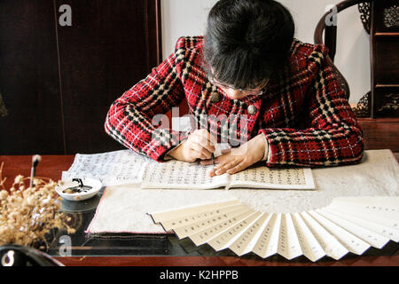 Hangzou, China - Mai. 22, 2016: Frau Mai ist schreiben Sie die chinesischen Symbole auf handgemachte Ventilator Stockfoto
